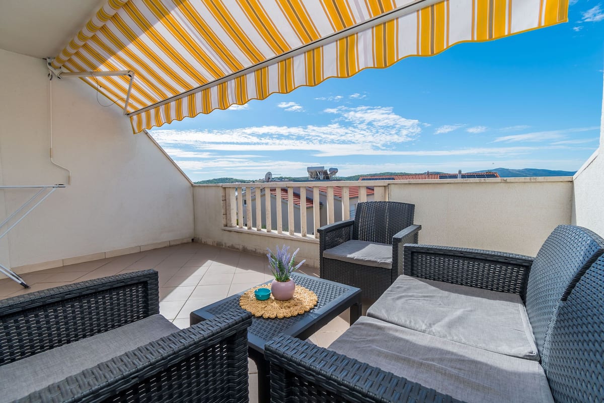 A balcony with wicker furniture, a striped awning, and a view of the cityscape.
