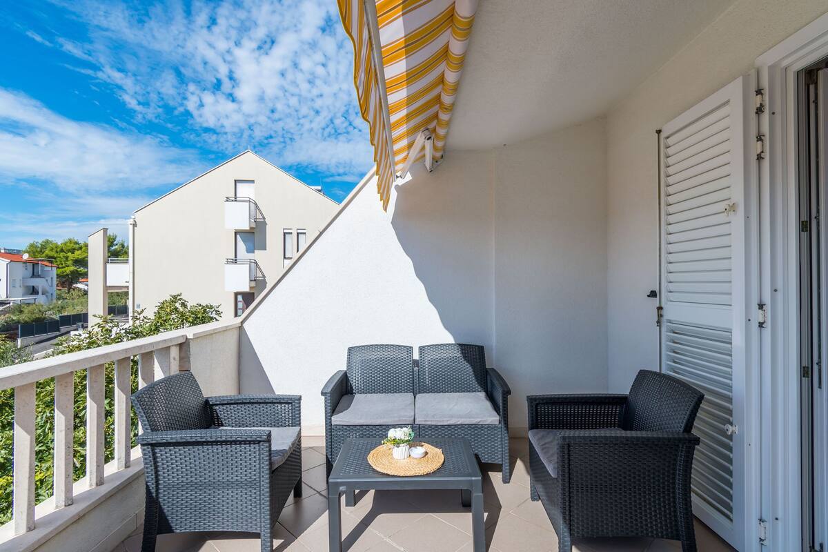 A balcony with a sofa, two chairs, and a table with a placemat and a small vase.