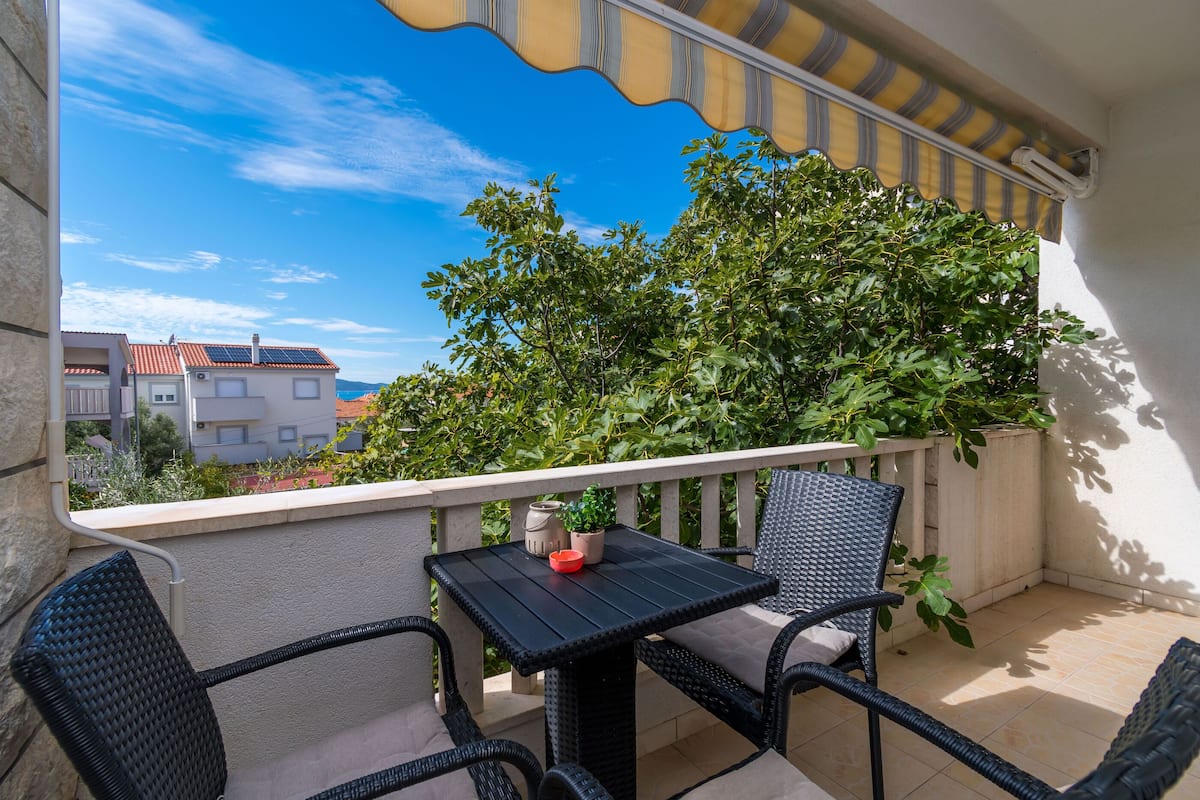 A balcony with a table and chairs, a potted plant, and a view of buildings and trees.