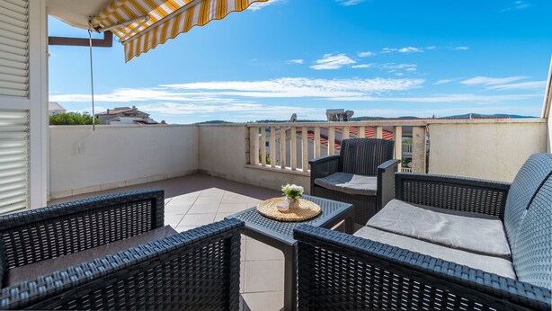 A balcony with wicker furniture, a striped awning, and a view of distant buildings. - Apartments Tily (Okrug Gornji)
