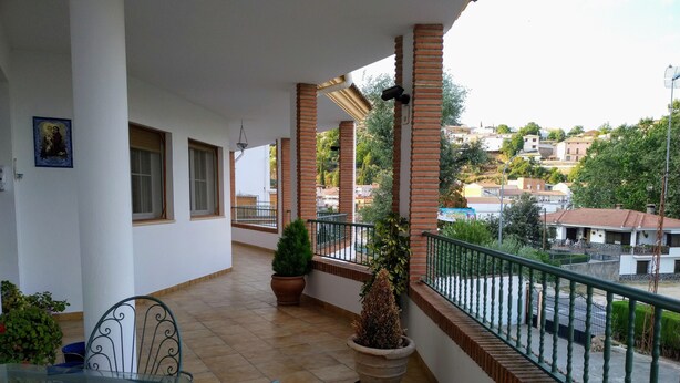 Un balcón con una mesa y sillas de vidrio, plantas en macetas y vistas del vecindario.