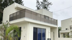 Ein modernes, zweistöckiges Haus mit Flachdach, großen Schiebeglastüren und einem Balkon mit Metallgeländer.