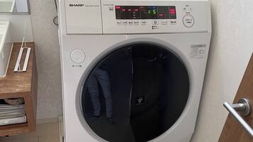 Eine kompakte, weiße Waschmaschine mit Frontlader und digitaler Anzeige, platziert in einer Ecke eines Zimmers mit strukturierter Tapete und einem Holzschrank.