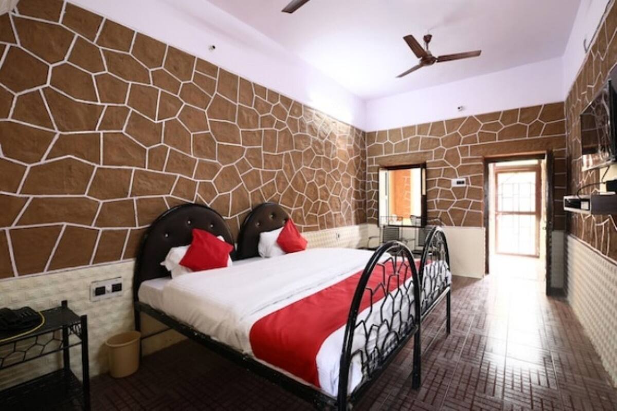 A bedroom with a stone wall, a bed with a red and white bedspread, a ceiling fan, and a window.