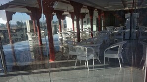A glass-enclosed outdoor dining area with white plastic chairs and red pillars. - Rawat Resorts (Tivari)