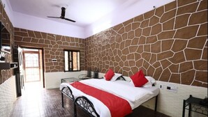 A bedroom with a stone wall, a bed with red and white bedding, a ceiling fan, and a brick floor. - Rawat Resorts (Tivari)