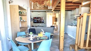 Un ambiente accogliente con zona pranzo, un tavolo rotondo e sedie blu, una cucina con televisore e una scala che conduce a un piano superiore.