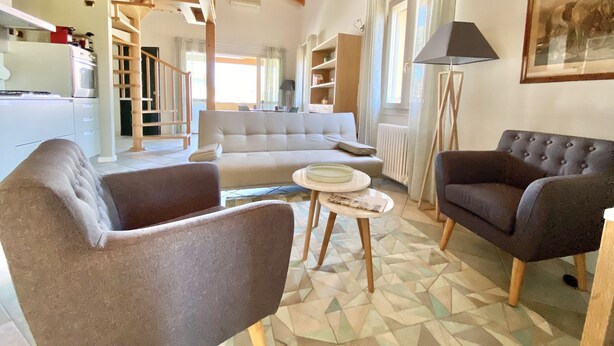 Un'ampia zona giorno con soffitto alto, travi in legno, un divano, due poltrone, un tavolino da caffè e un pavimento a motivo geometrico.