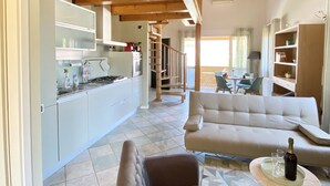 Un'ampia zona giorno con soffitto in legno a vista, un divano, un tavolo da pranzo e una cucina sullo sfondo.