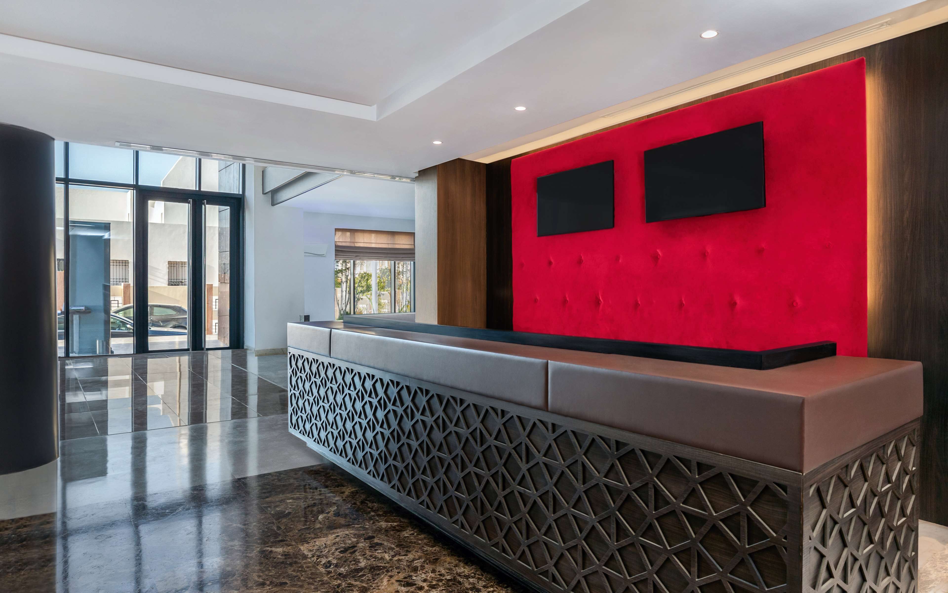 A reception area with a red accent wall, a modern reception desk, and a glass door leading outside.