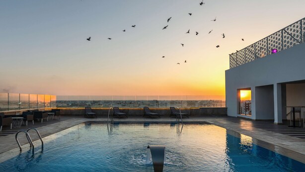 A rooftop pool with lounge chairs and a view of the city skyline at sunset. - Hotel Sfax Palace by Plaza Hotels & Resorts (Sfax)