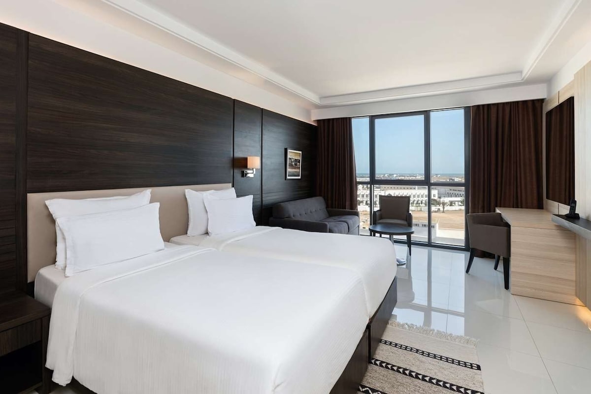 Una habitación de hotel moderna con una cama grande, una zona de estar y vistas a la ciudad.