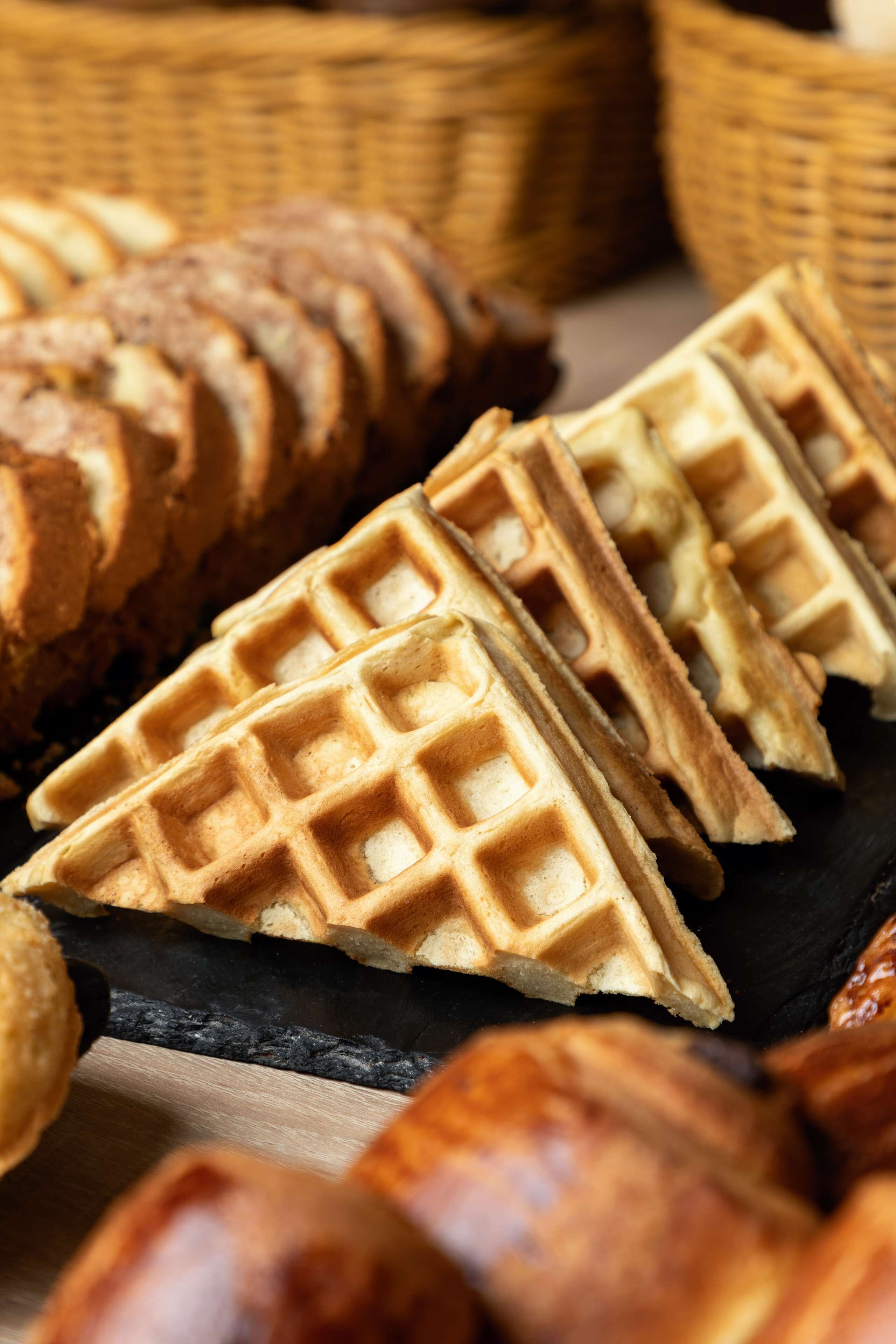 Gros plan sur des gaufres fraîchement préparées, à la croûte dorée, disposées sur une planche d’ardoise sombre.