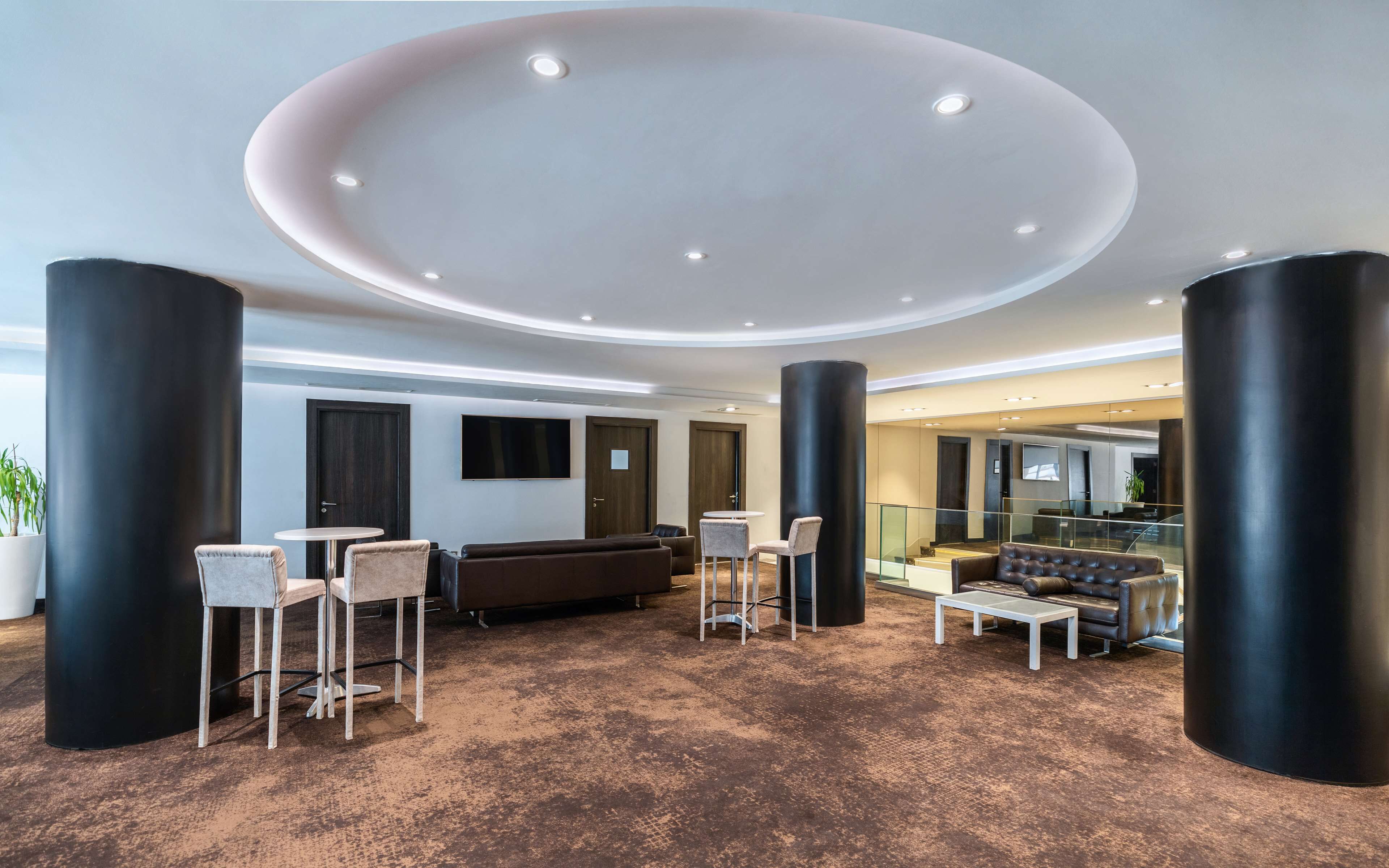 A modern lobby with a circular ceiling design, black columns, and a mix of seating options including a sofa and chairs.