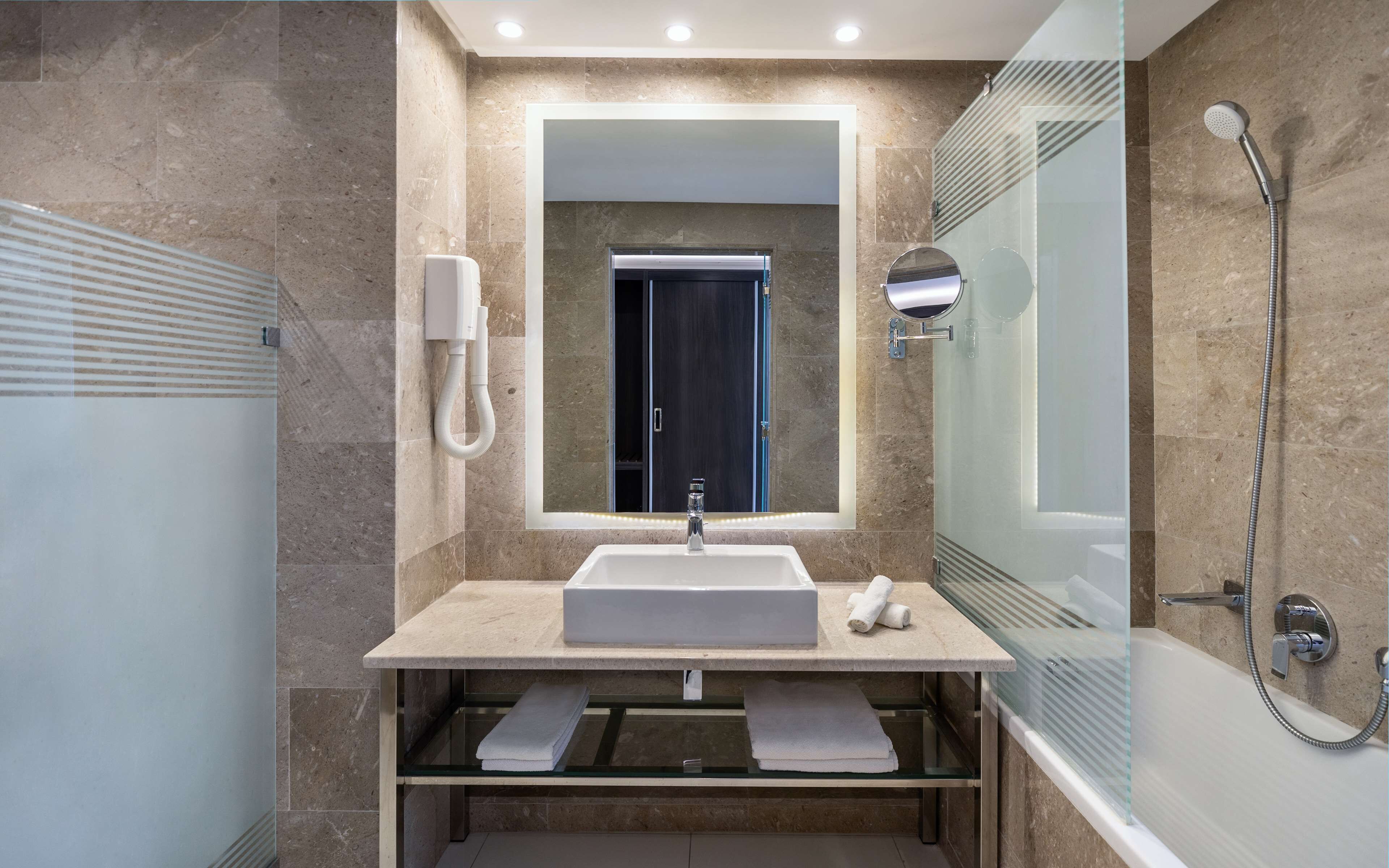 A modern bathroom with a large mirror, a sink, a glass-enclosed shower, and a built-in towel rack.