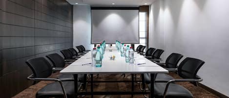 Un salón de conferencias con una larga mesa, sillas negras y botellas de agua.