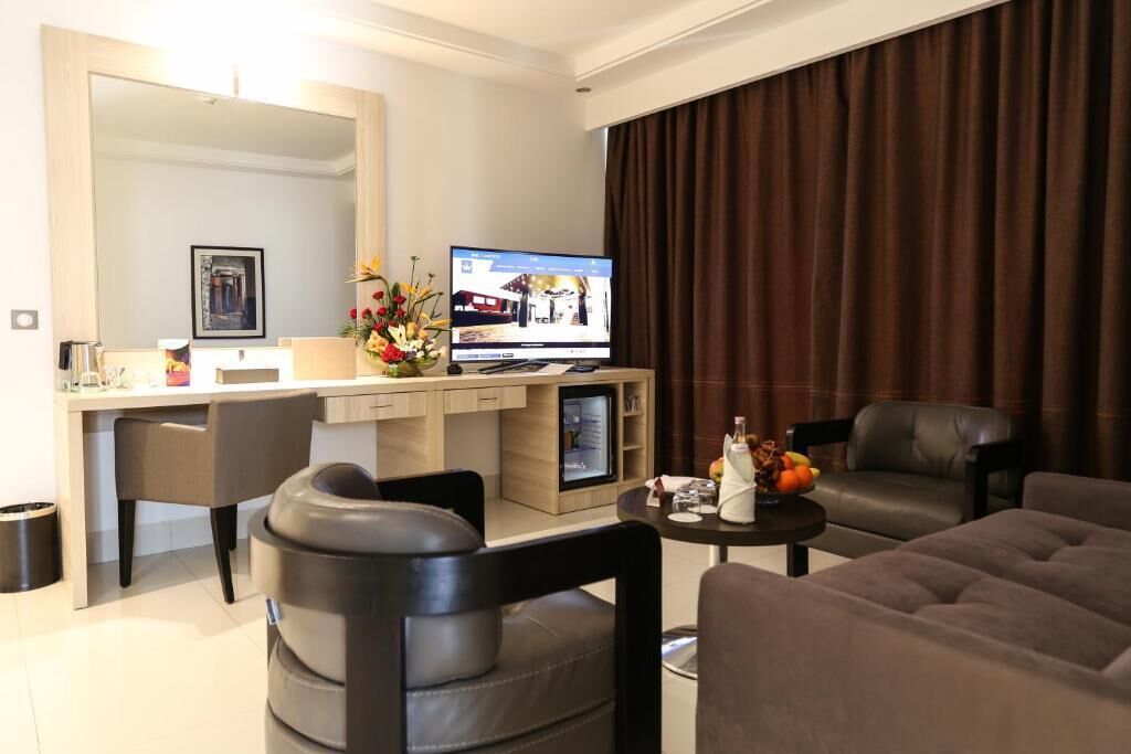 A modern hotel room with a flat-screen TV, a desk, a sofa, and a dining area.