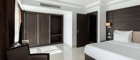 Habitación de hotel moderna con una cama grande, un escritorio con silla, un armario y un baño visible a través de una puerta abierta.