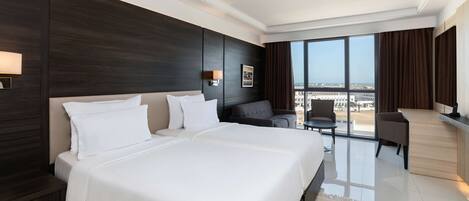 A modern hotel room with a large bed, a seating area with a view, and a balcony with a cityscape view.