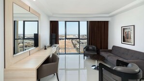 A modern living room with a large window, a sofa, a desk, and a television. - Hotel Sfax Palace by Plaza Hotels & Resorts (Sfax)
