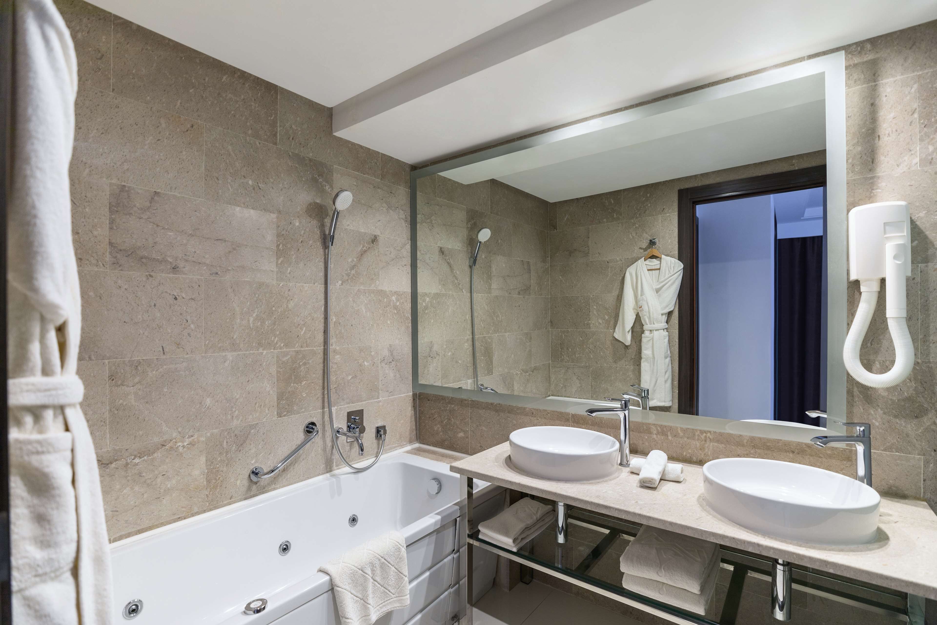 Un baño moderno con bañera, dos lavamanos, un espejo grande y un perchero para toallas.