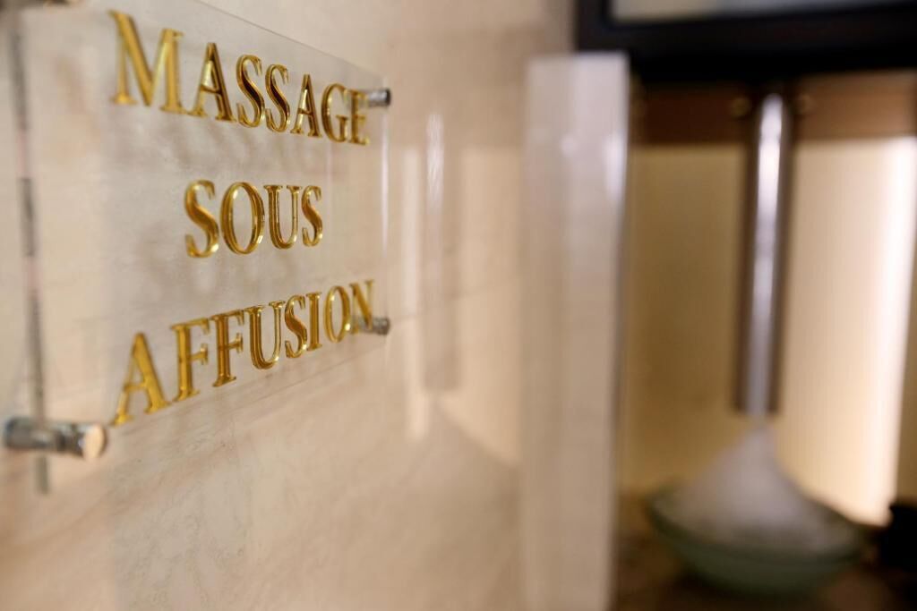 A sign with the words "MASSAGE SOUS AFFUSION" on a marble wall.