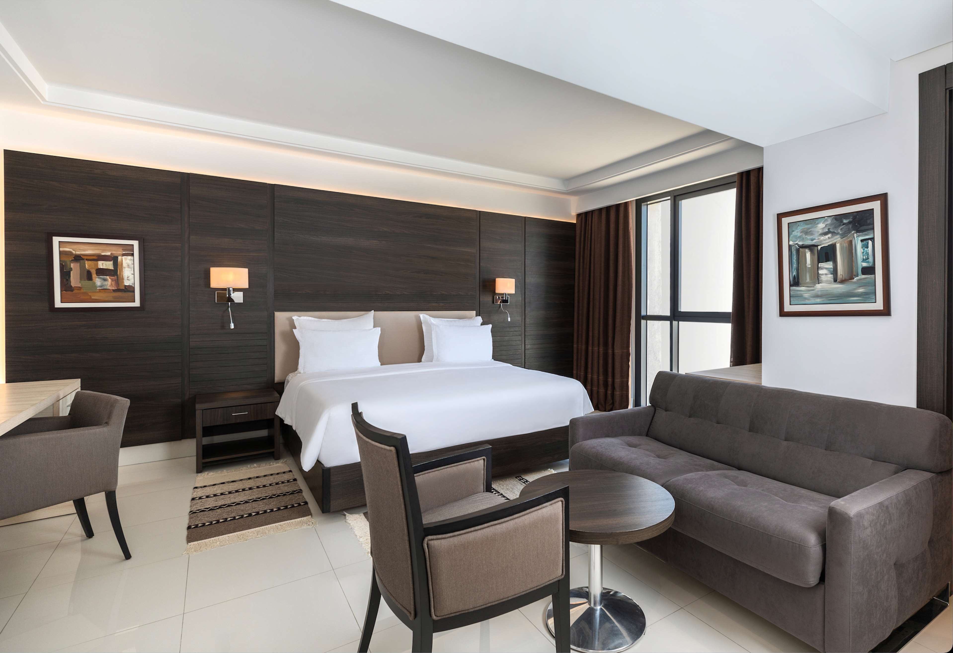 A modern hotel room with a large bed, a sofa, a desk, and a small table.