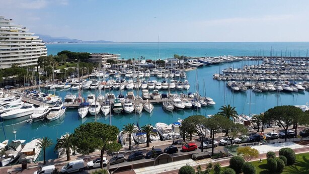 A marina with numerous boats docked, a large hotel building, and a clear view of the sea.