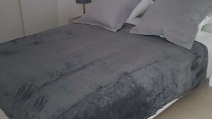 A bed with a grey bedspread and pillows, a bedside lamp, and a white headboard.