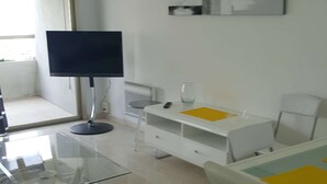 A modern room with a glass table, white furniture, a standing lamp, and a TV.