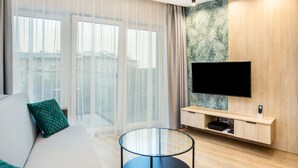 Ett modernt hotellrum med en stor säng, ett soffbord i glas, en platt-TV som är monterad på en vägg av trä och en skjutdörr i glas som leder ut till en balkong.