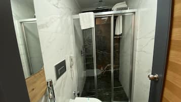 A compact bathroom with a toilet, a glass-enclosed shower, and a marble-tiled wall.