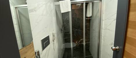 A compact bathroom with a toilet, a glass-enclosed shower, and a marble-tiled wall.