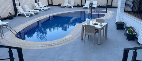 Zona de piscina en la azotea con sillones de descanso, una mesa y plantas en macetas.