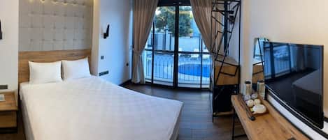 Camera d'hotel con un letto grande, una televisione, una scrivania con un computer e un balcone vista piscina.