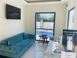 Una sala moderna con un sofá azul aguamarina, un sofá blanco y una mesita. Se aprecia una ventana grande con vistas a una piscina y un área de estar al aire libre.