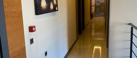 Pasillo de hotel con panel de madera, letrero de número, detector de incendios y una obra de arte enmarcada.