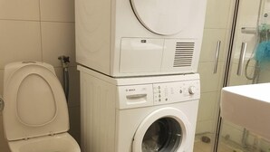 Un bagno compatto con il water, una lavatrice e asciugatrice impilate e un box doccia in vetro.