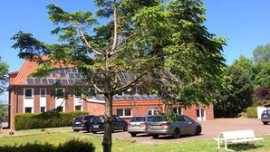 A building with a red brick facade, solar panels on the roof, and parked cars in the driveway.