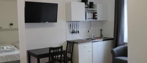 A compact hotel room with a kitchenette, a bed, a TV, and a seating area.
