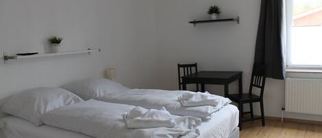 Un dormitorio con cama, mesita de noche, silla y ventana con cortinas.