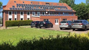 A building with a red brick facade, solar panels on the roof, and a parking lot with several cars.