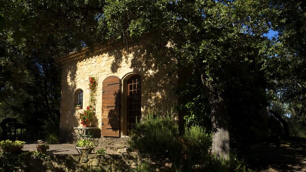 A stone building with arched windows, surrounded by lush greenery and trees. - L'Atelier, with its century-old oak trees and panoramic view of the Luberon region (Cucuron)