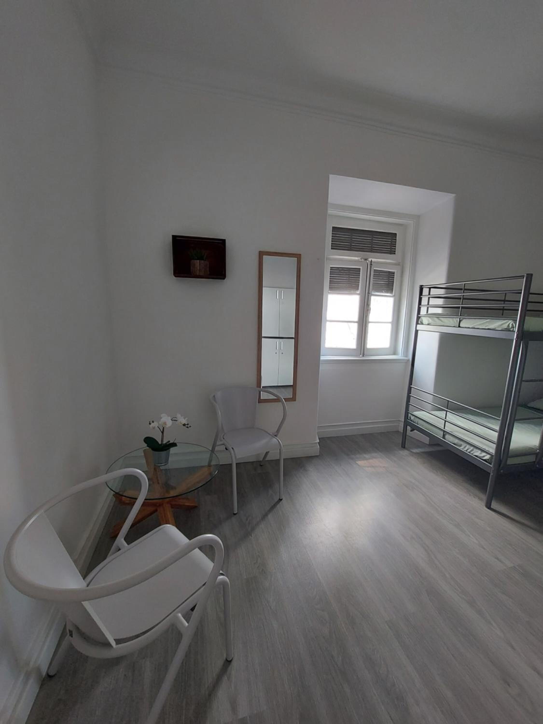 Une chambre avec un lit superposé, une chaise, une petite table avec une plante et un miroir au mur.
