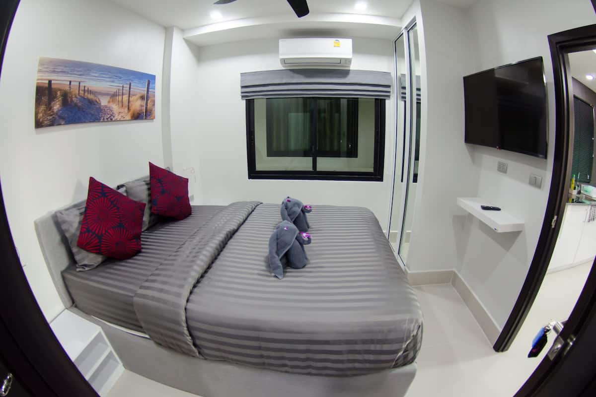 A modern bedroom with a bed, two pillows, a window, an air conditioner, a TV, and a painting on the wall.
