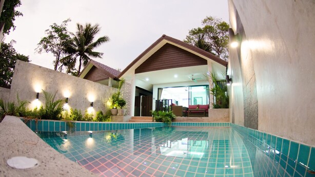 A swimming pool with a tiled deck, a covered patio area, and a view of a building with a sloped roof. - The Elegance Pool Villas at KP Beach (Ko Chang)