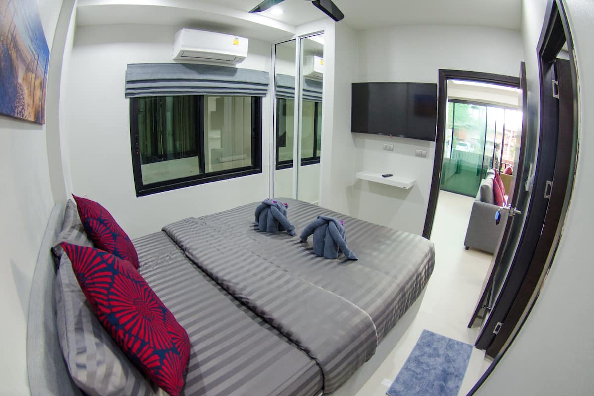 A hotel room with a bed, a TV, a mirror, and a window.
