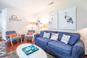 A living room with a blue sofa, two armchairs, a coffee table, wall art, and a clock.