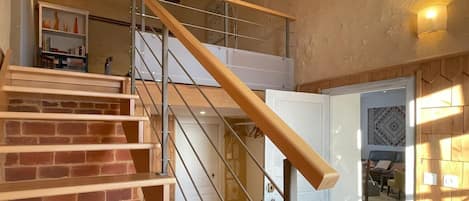 Una escalera con escalones de madera y barandillas de metal, que sube a un piso superior.