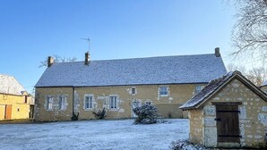 A two-story stone house with a sloped roof, a small attached shed, and a snow-covered yard.